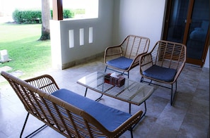 A patio with wicker furniture, a glass table, and a view of the garden. - Modern Coastal Living (As Sifah)