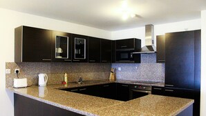 Eine moderne Küche mit Granitarbeitsplatten, dunklen Schränken, einer eingebauten Mikrowelle und einer Edelstahl-Dunstabzugshaube.