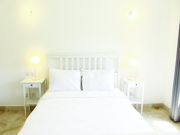A white bed with two pillows, two bedside tables, and two wall-mounted lamps.