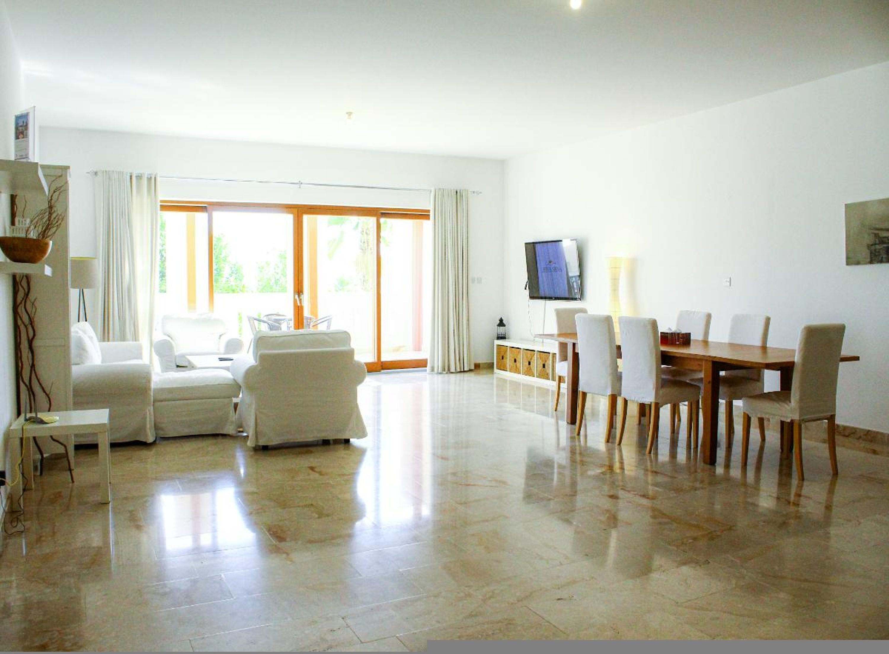 A spacious living area with a sofa, chairs, a dining table, and a TV.