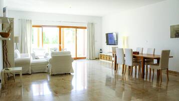 A spacious living area with a sofa, chairs, a dining table, and a TV.