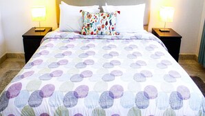 A hotel room with a bed, two bedside tables, two lamps, and a colorful pillow.