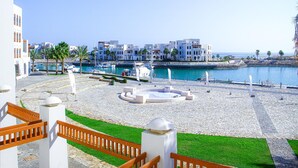 A coastal promenade with a marina, white buildings, and a clear blue sky.