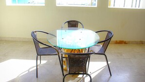 A round glass table with four wicker chairs in a room with large windows.