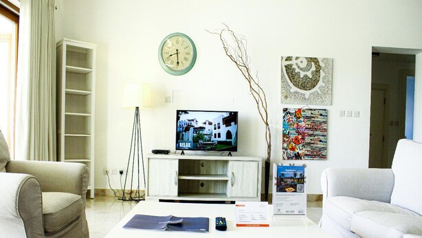 A living room with a television, a clock, a bookshelf, and a poster on the wall.