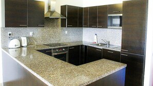 A modern kitchen with dark cabinetry, granite countertops, a built-in oven, and a microwave.