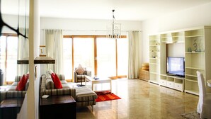 A modern living room with a sofa, armchair, coffee table, and a TV on a stand. - Modern 2-bedroom With Marina Views (As Sifah)