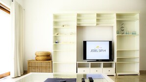 A living room with a flat-screen TV, white shelving units, a glass coffee table, and a wicker basket. - Modern 2-bedroom With Marina Views (As Sifah)