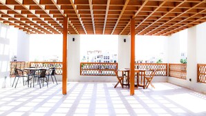 An outdoor patio with a wooden pergola, tables, chairs, and a view of buildings in the background. - Modern 2-bedroom With Marina Views (As Sifah)