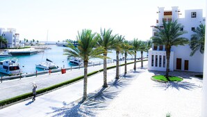 A coastal marina with boats, palm trees, and a white building with balconies. - Modern 2-bedroom With Marina Views (As Sifah)