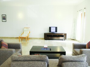 Ein Wohnzimmer mit einer Sofagarnitur, einem Holzstuhl, einem Fernseher auf einem Holzschrank und einem Couchtisch.