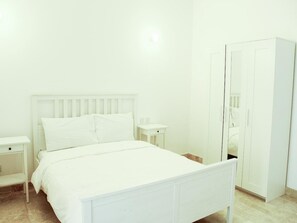 Ein heller Raum mit einem Bett, einem Nachttisch, einem Kleiderschrank und einem Spiegel.