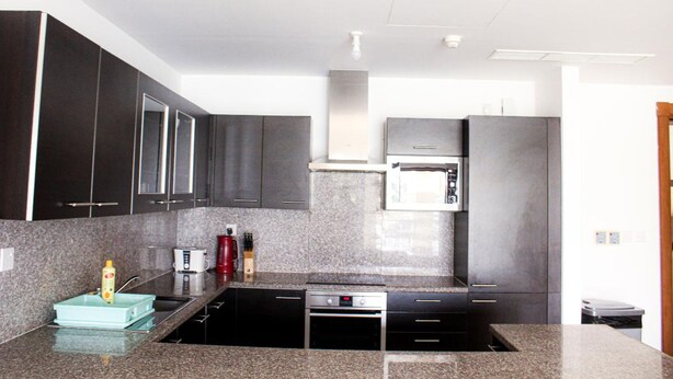 A modern kitchen with dark cabinets, a built-in oven, and a granite countertop. - Elegant Coastal Living (As Sifah)