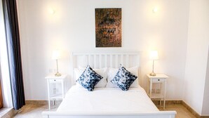 A white four-poster bed with two nightstands, each with a lamp, in a room with a large abstract painting above the bed. - Elegant Coastal Living (As Sifah)