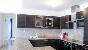 A modern kitchen with dark cabinetry, granite countertops, and stainless steel appliances. - Elegant Coastal Living (As Sifah)