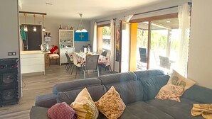 Ein modernes Wohnzimmer mit Sofa, Essbereich, Küche und großen Schiebeglasüren zum Balkon.