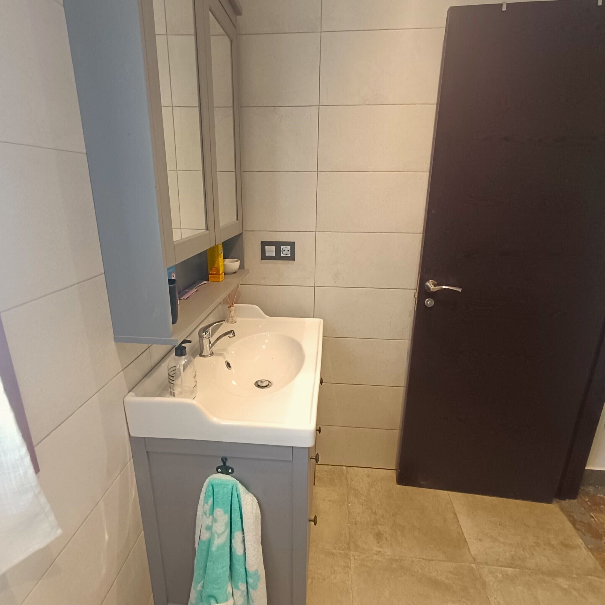 A bathroom with a white sink, a mirror, a towel hanging on a rack, and a door.