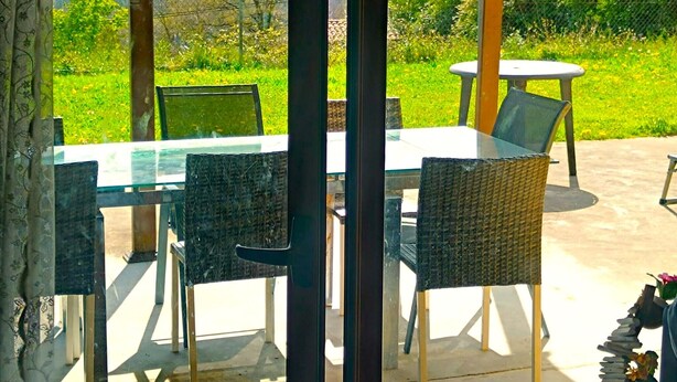 Eine Terrasse im Freien mit Tisch und Stühlen, einer Pergola und Blick auf eine grüne Landschaft.