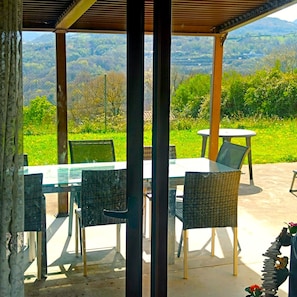 Une terrasse extérieure avec une table et des chaises, une pergola et une vue sur un paysage verdoyant.