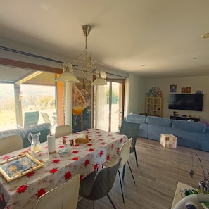 Un coin repas avec une table dressée pour quatre personnes, un lustre et une vue dégagée sur l’extérieur grâce à une grande fenêtre.