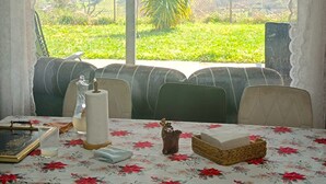 Ein Essbereich mit Tisch für zwei, Blick auf eine grüne Landschaft und einer Decke mit freiliegenden Balken und Pendelleuchten.