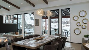 Een moderne eethoek met een grote tafel voor zes personen, grote ramen met uitzicht op sneeuw en een bijzondere plafondlamp.