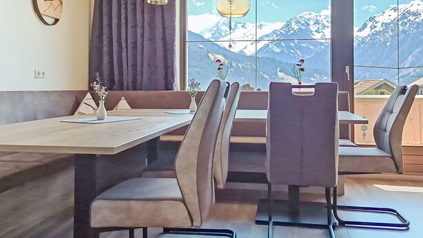 A dining area with a table, chairs, a clock, and a view of mountains. - Panoramablick Tauern by Interhome (Mittersill)