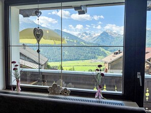 Une fenêtre donnant sur les montagnes, un parapluie jaune et deux vases de fleurs.