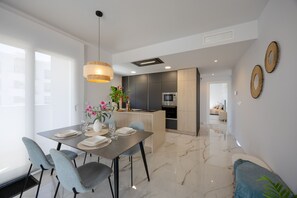 Et moderne køkken med mørke skabe, en central ø og et spiseområde med et bord dækket til fire.