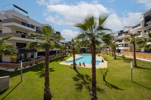 A modern hotel with a swimming pool surrounded by palm trees and a well-maintained lawn. - Casa Alegria – Oasis of Light, Terrace and Wellness on the Costa Blanca (Orihuela Costa)