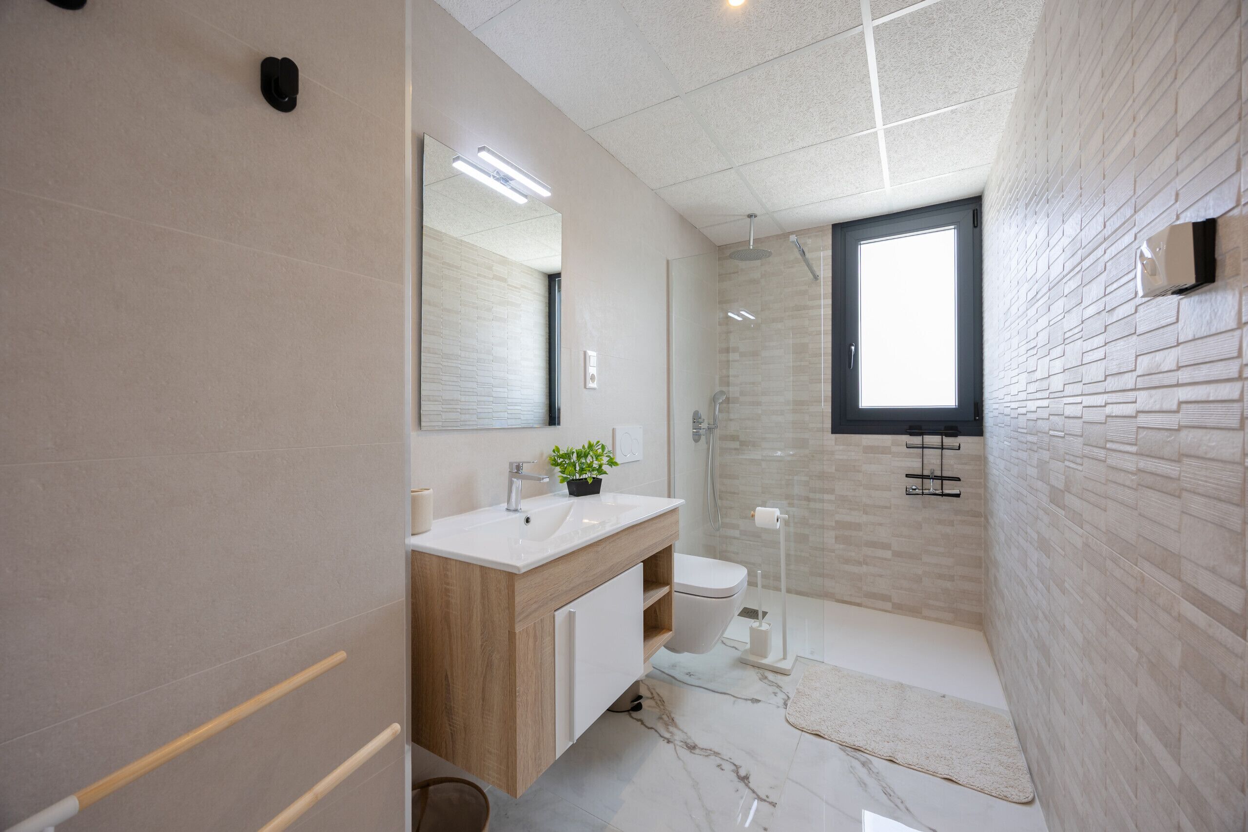 A modern bathroom with a wooden vanity, a large mirror, a shower, and a window.