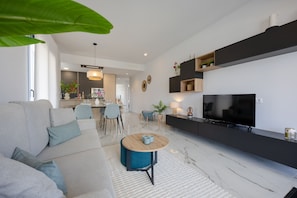 A modern living room with a sofa, coffee table, TV, and a dining area in the background. - Casa Alegria – Oasis of Light, Terrace and Wellness on the Costa Blanca (Orihuela Costa)