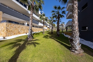 A modern building with balconies, palm trees, and a stone wall. - Casa Alegria – Oasis of Light, Terrace and Wellness on the Costa Blanca (Orihuela Costa)