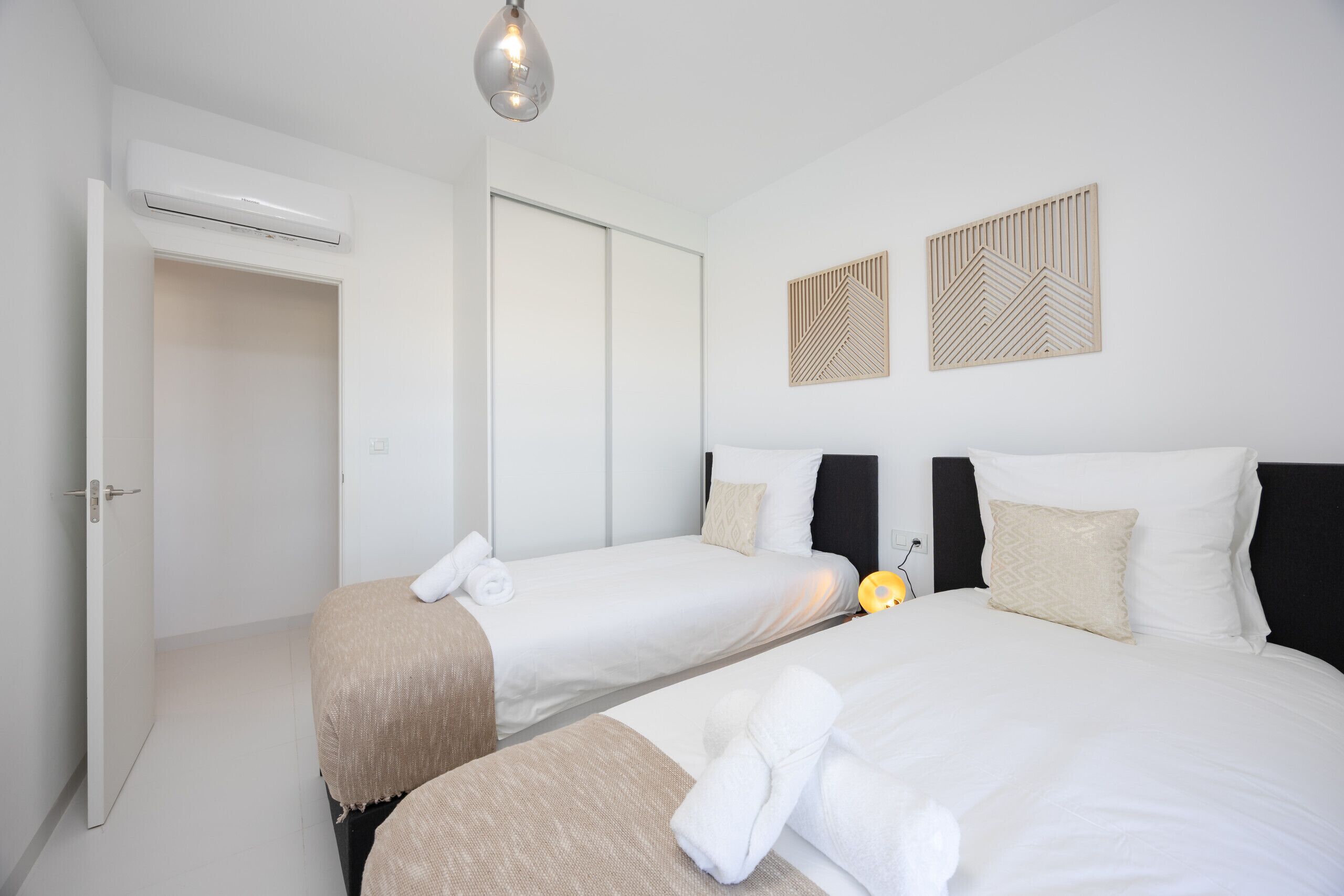 A hotel room with two beds, an air conditioning unit, a door, and two wall-mounted decorative panels.