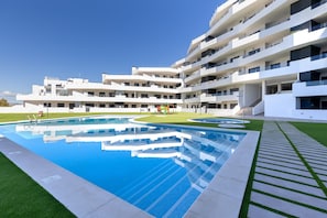 Ein modernes Gebäude mit Pool, mehreren Balkonen und einem gepflegten Rasen.