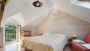 A bedroom with a sloped ceiling, wooden walls, a bed with a leaf-patterned bedspread, a red sofa, and a small bedside table with a lamp. - Guest Room “Les Hirondelles” with Shared Terrace, Communal Garden and Wi-Fi (Cancale)