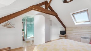 Ein Schlafzimmer mit schräg steilender Decke, einem Bett mit blattgemustertem Überwurf, einem Fernseher und einem Fenster.