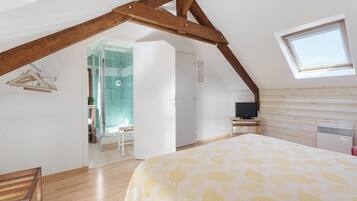 Ein Schlafzimmer mit schräg steilender Decke, einem Bett mit blattgemustertem Überwurf, einem Fernseher und einem Fenster.