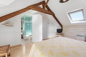 Ein Schlafzimmer mit schräg steilender Decke, einem Bett mit blattgemustertem Überwurf, einem Fernseher und einem Fenster.