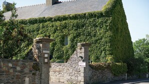 Un edificio de piedra con techo empinado, paredes cubiertas de hiedra y un letrero que dice 'Chambres Dits de Vignes'.