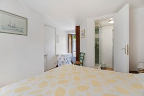 Ein Schlafzimmer mit Bett, Stuhl, Tisch und einem durchgehenden Türspalte sichtbaren Badezimmer.