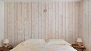 Un dormitorio con pared de listones de madera, cama con colcha estampada con motivos de hojas, dos mesitas de noche con lámparas y una decoración con forma de corazón en la pared.