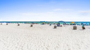 Ein Strand mit weißem Sand, Sonnenschirmen und Menschen.