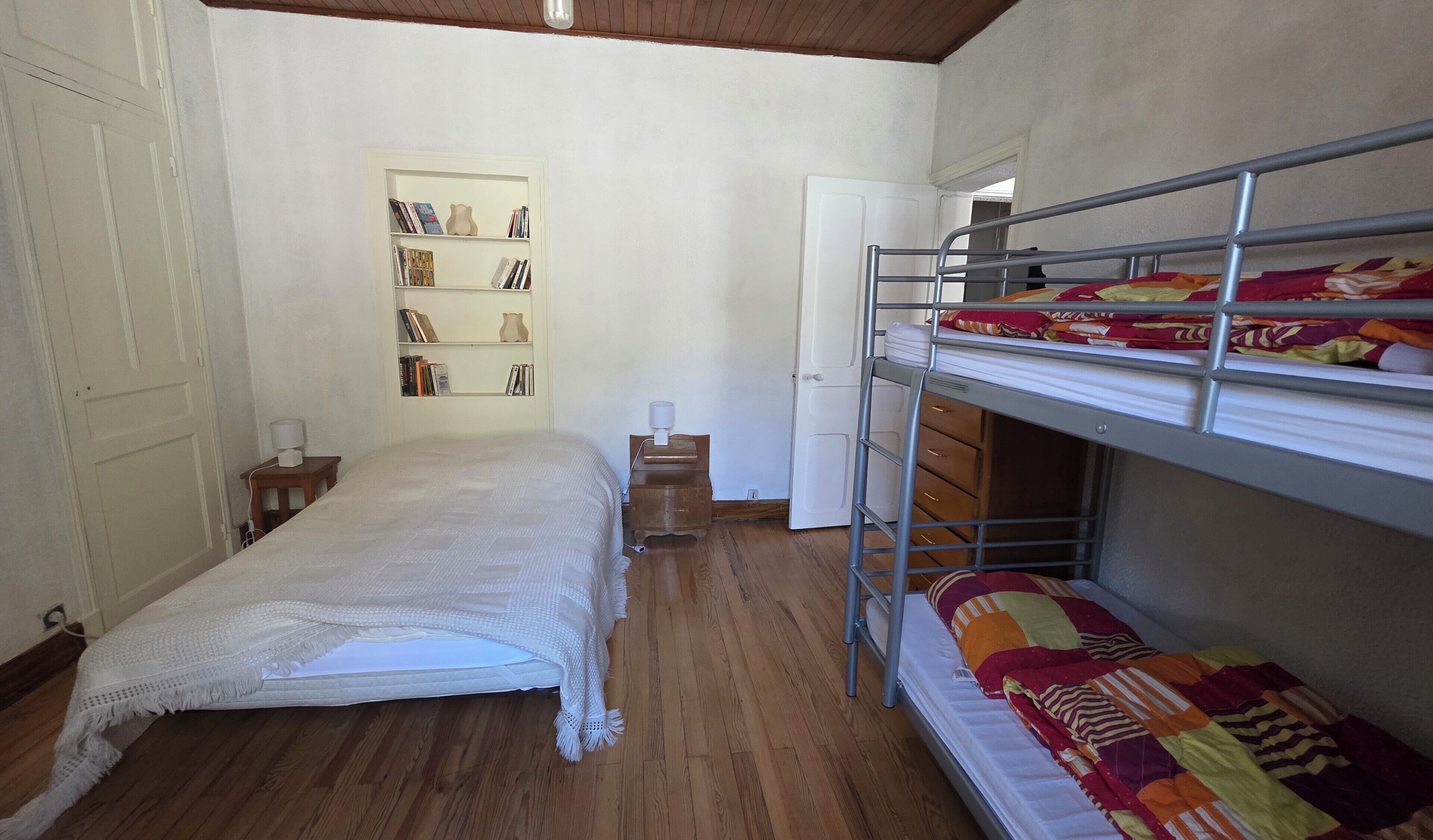Ein Zimmer mit Etagenbett, Einzelbett, Bücherregal und einer Tür.