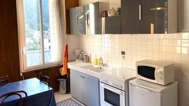 Keittiössä on valkoiset kaapit, mikroaaltouuni, uuni, pesuallas sekä ruokapöytä tuoleineen.
