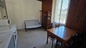 Keittiössä on mikroaaltouuni, pesukone, puinen ruokapöytä tuoleineen, kuviollinen sohva ja puinen kirjahylly.