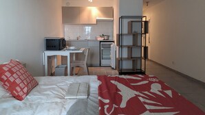 Ein kompaktes Zimmer mit Bett, Schreibtisch, Küchenzeile und einer fest eingebauten Bücherablage.