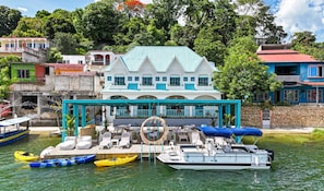 Una propiedad frente al mar con una casa grande, un espacio de estar al aire libre cubierto y varios barcos.