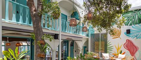 A courtyard with wicker furniture, potted plants, and a mural of leaves on the wall.