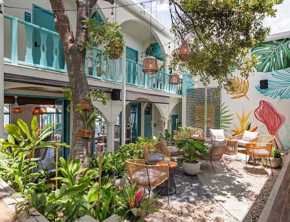Un patio con muebles de mimbre, plantas en macetas y un mural de hojas en la pared.